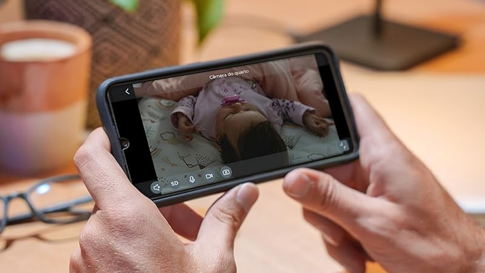 Casa inteligente Positivo: pai monitora bebê por celular, o qual reproduz imagens gravadas em tempo real por câmera com Wi-Fi — Foto: Reprodução/Amazon